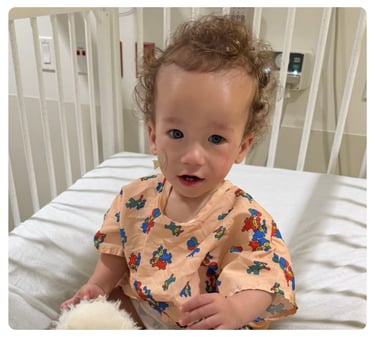 Young child wearing a patterned hospital gown sits on a hospital bed.