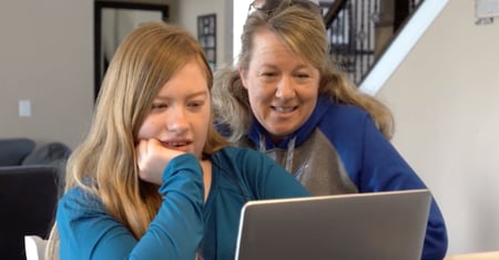A young woman and her mom look at a laptop together at a table.