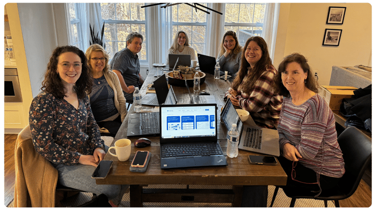 Seven members of the FPWR research team sit around a table with laptops during a meeting.