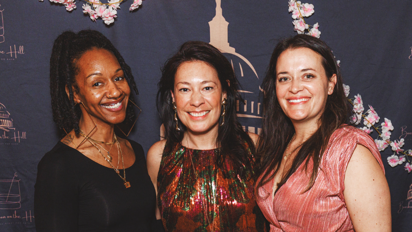 Three women smile and pose together at an indoor event.