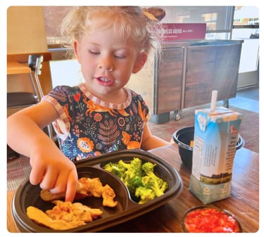 Young girl eating a meal with vegetables at a restaurant table.
