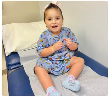 Young child smiling while sitting on an exam table in a medical gown.