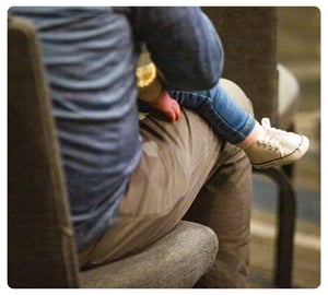 Young child wearing jeans and white sneakers sitting on an adult’s lap.