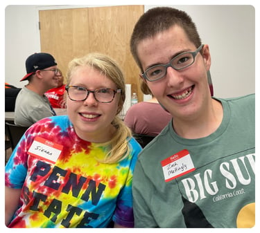 Two young people wearing glasses smiling together at an indoor event.