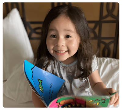 Young child smiling while looking at a colorful book.