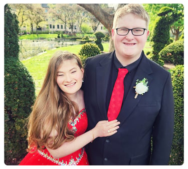 Young woman and young man dressed for a formal event, smiling together outdoors.