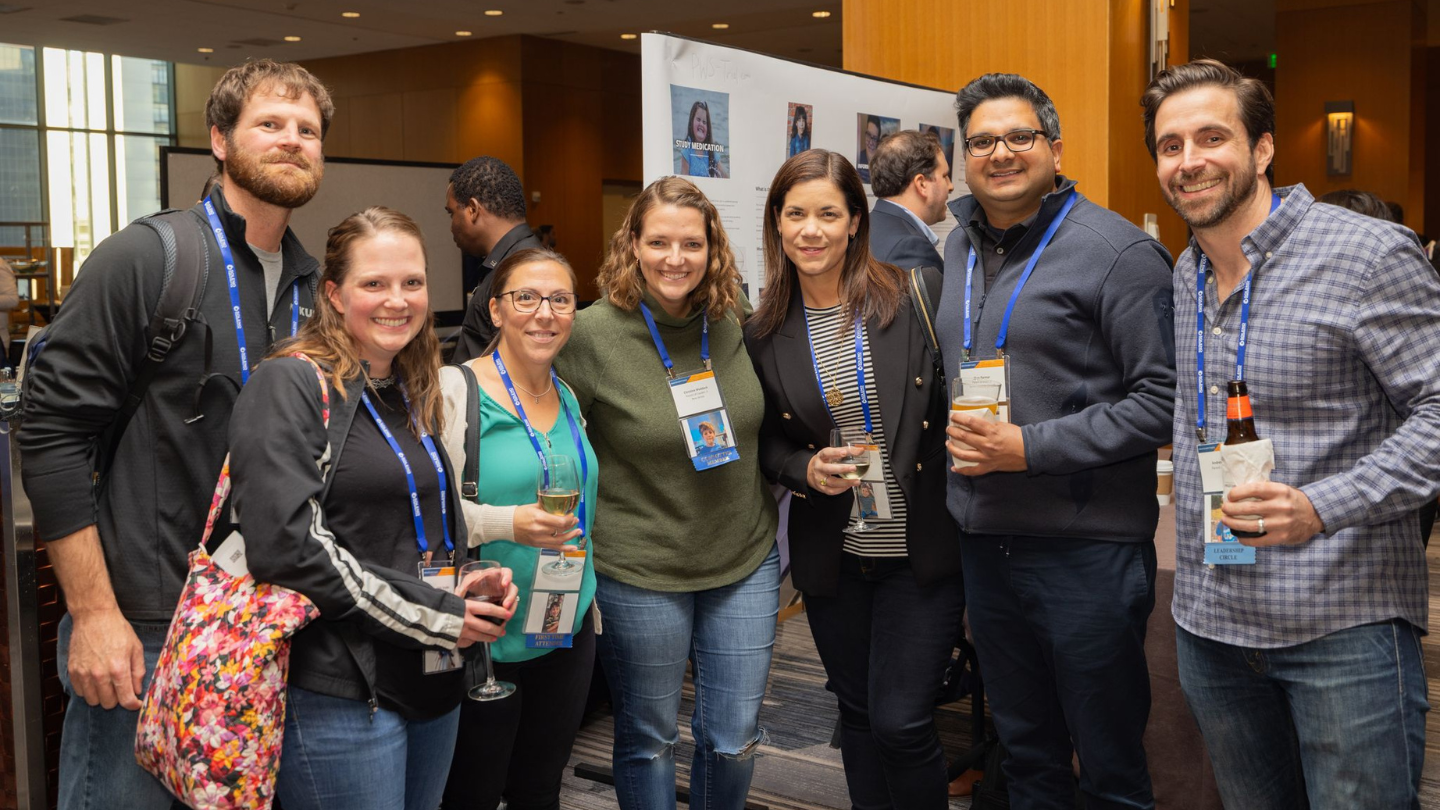 Seven FPWR conference attendees smile together during a reception, with research posters displayed behind them.