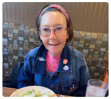 Woman wearing glasses and a denim jacket seated at a table with a meal.