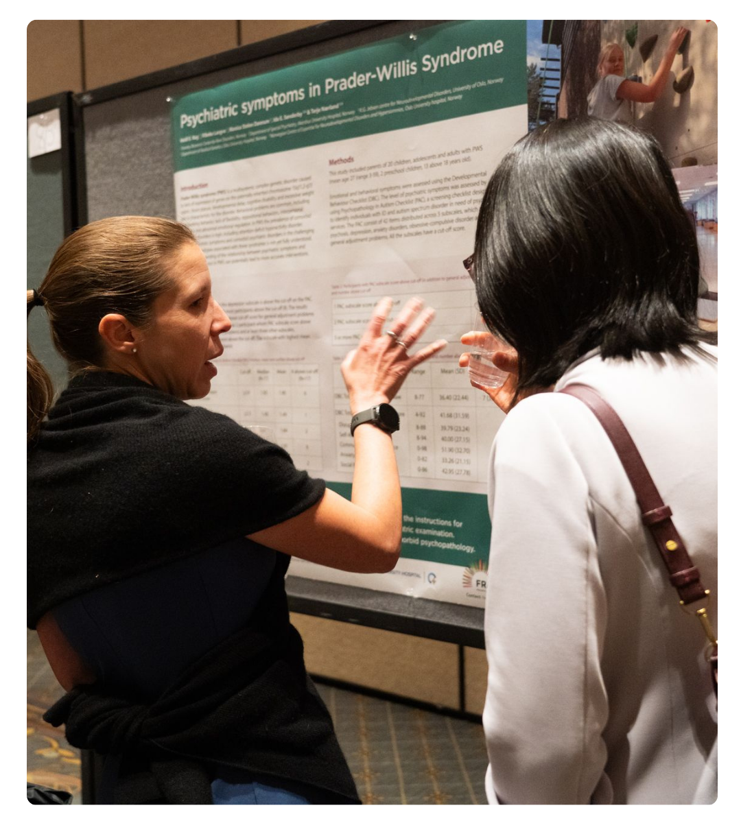 Two attendees discussing a research poster about psychiatric symptoms in Prader-Willi syndrome.