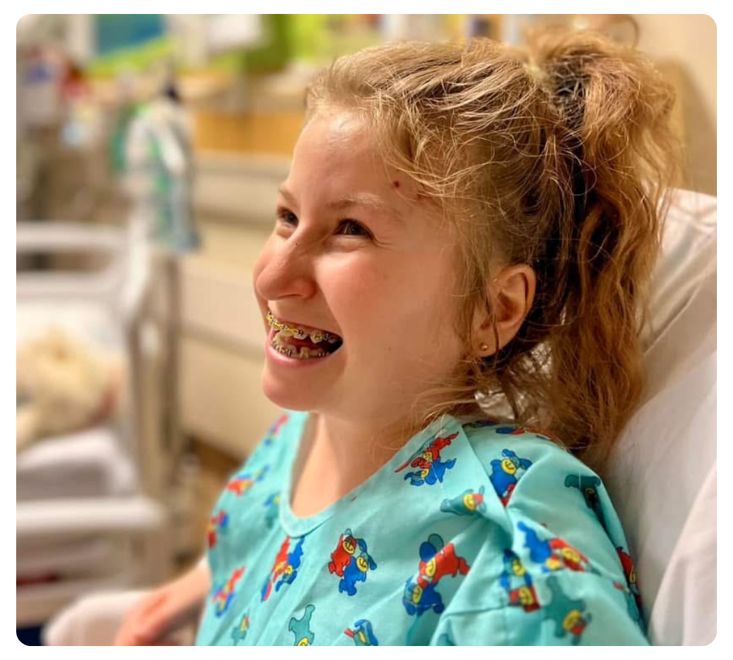 Young girl smiling in colorful hospital gown.