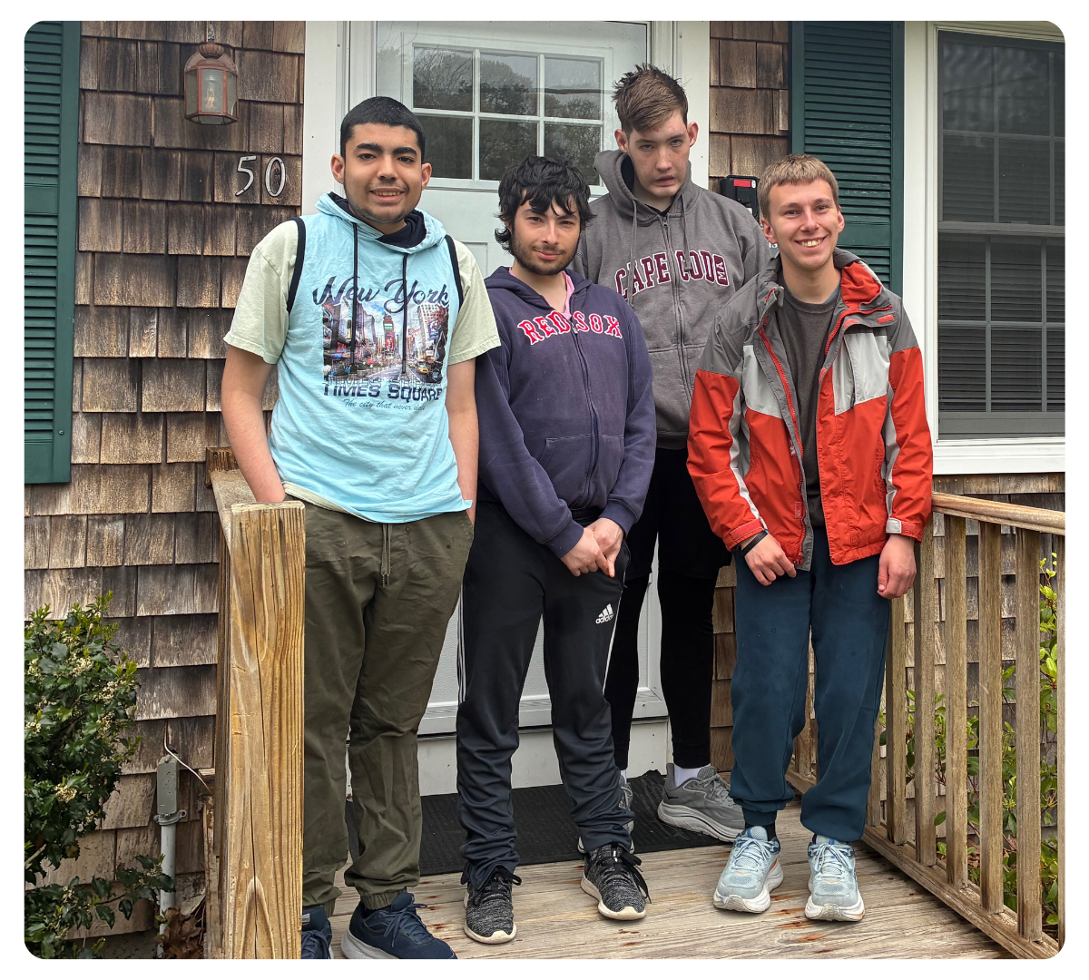 Four young men standing together outdoors in front of a house.