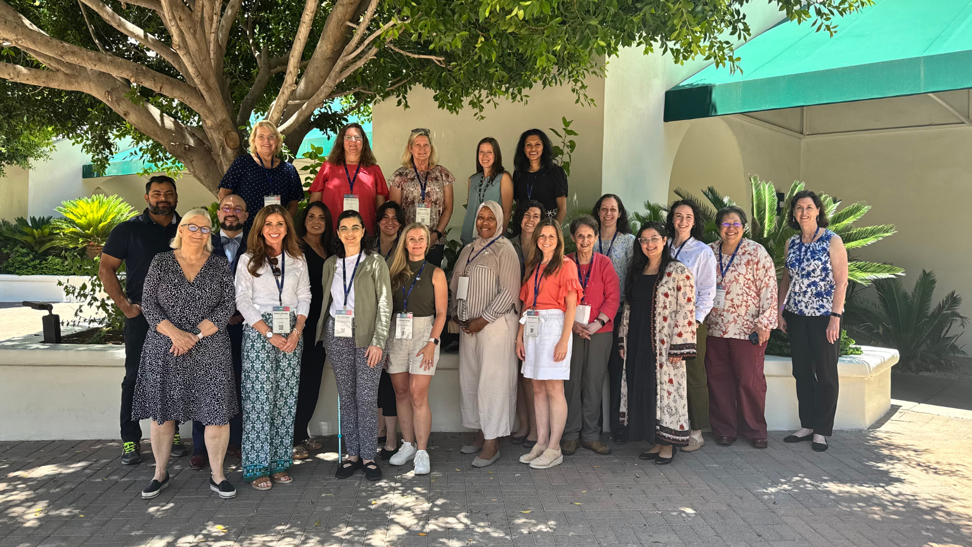 Group of PWS clinicians and researchers wearing conference badges pose together outdoors beneath a large tree.