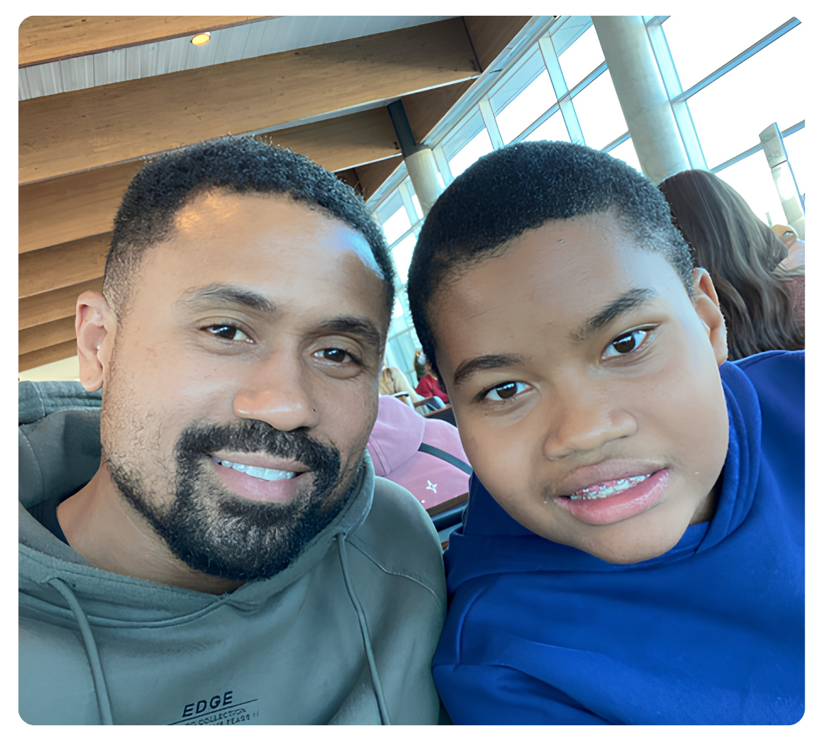 Adult man and young boy smile for a close-up selfie while seated indoors.