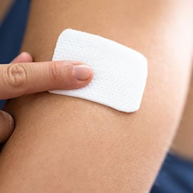 Close-up of a person applying an adhesive patch to their upper arm.