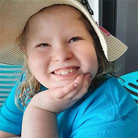 Smiling young girl in a sunhat and turquoise shirt rests her chin on her hand.