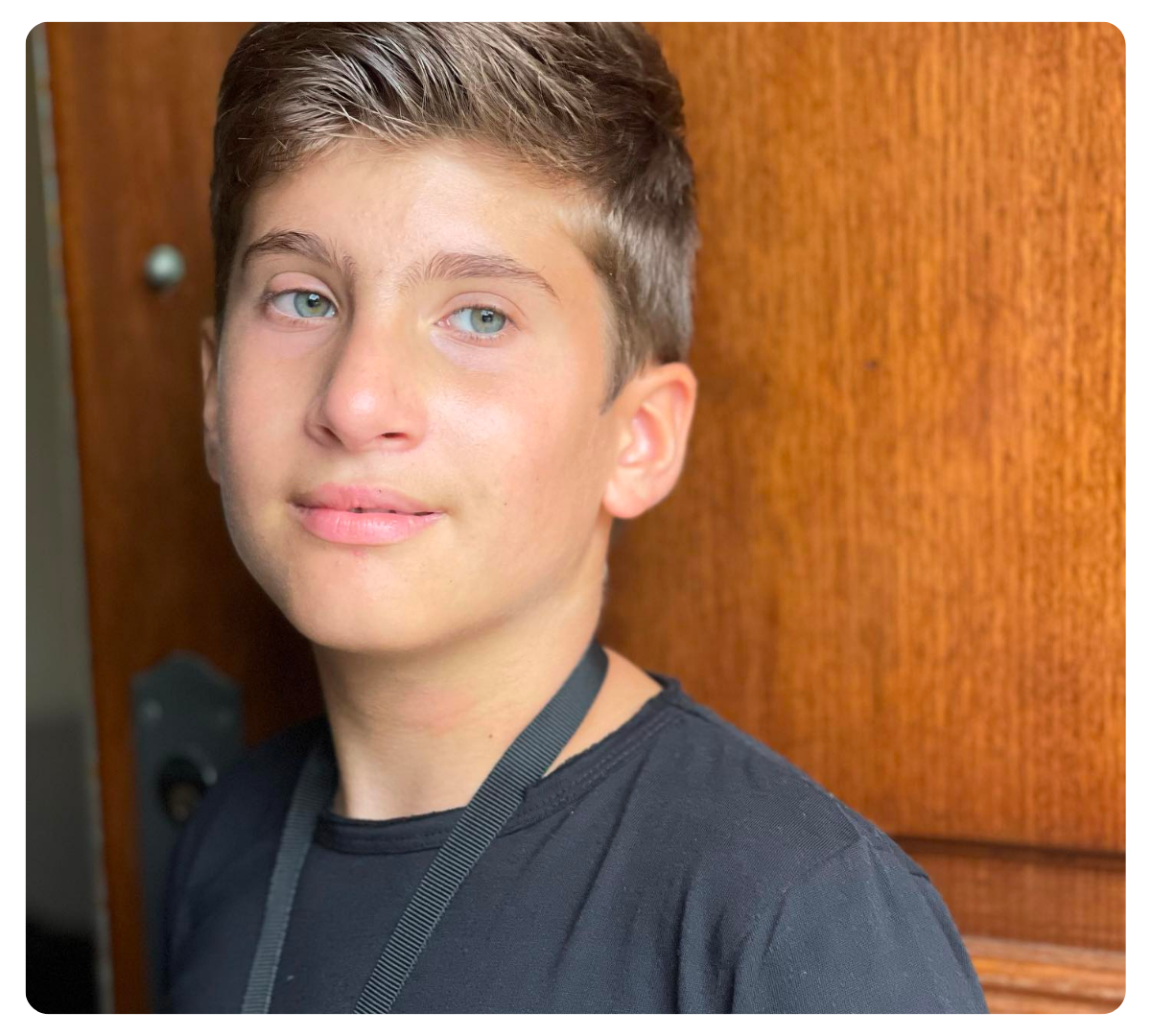 Close-up portrait of a teenage boy standing in front of a wooden door.