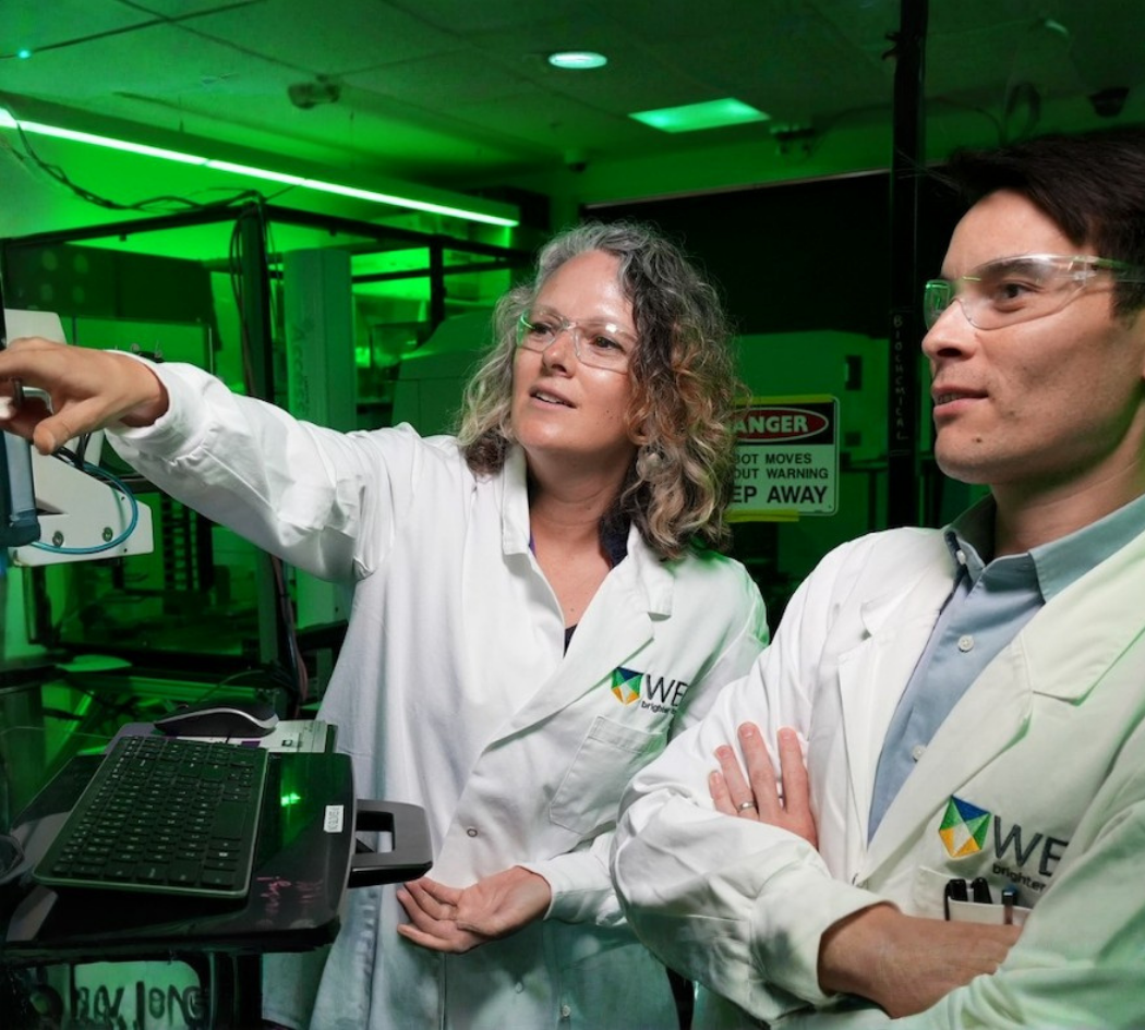 Two researchers wearing safety glasses and lab coats working together in a laboratory.
