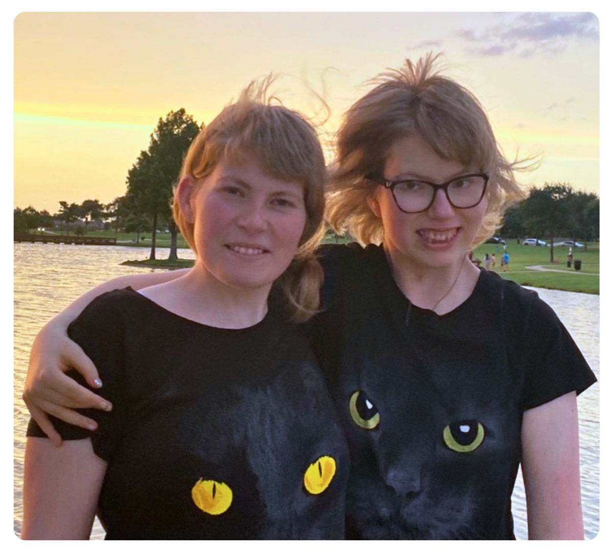 Two young people smiling with their arms around each other outdoors at sunset.